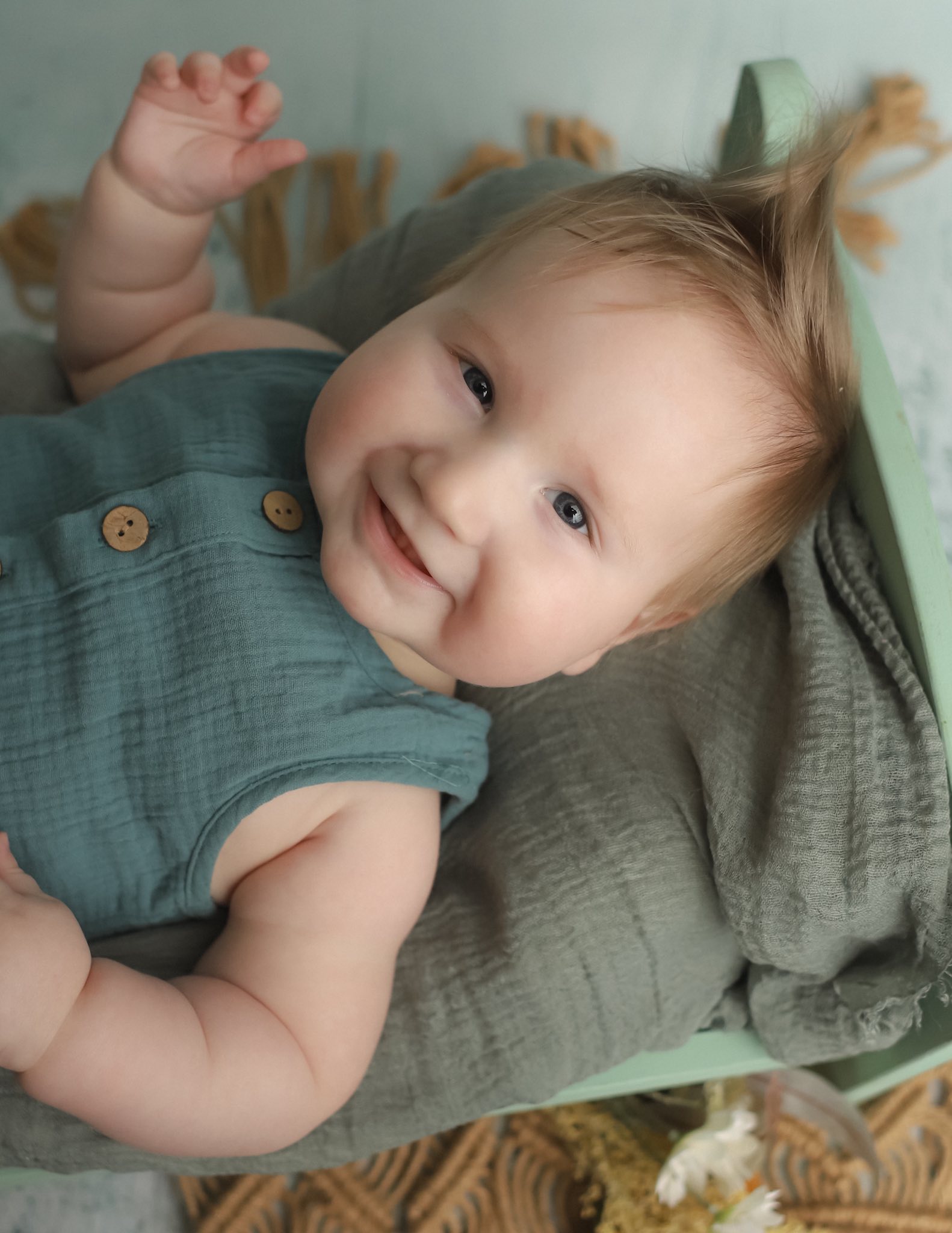 Smiling baby in a sage-green romper during a six-month sitter session