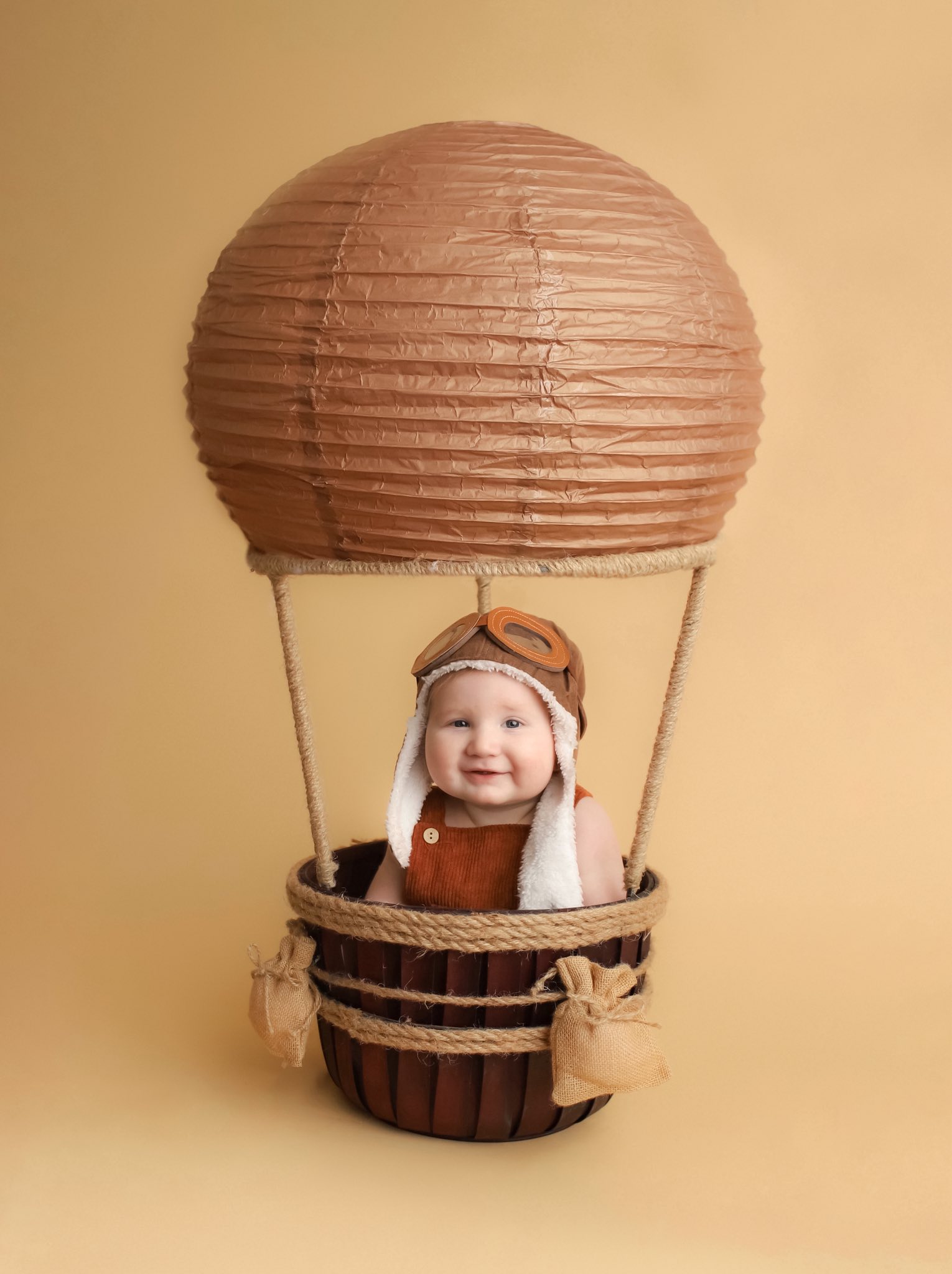 Baby in an aviator cap seated in a hot-air-balloon themed setup